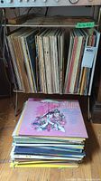 Photo of vinyl records stored vertically on a metal rack and a stack on the floor underneath.
