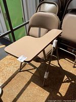 Front view of one steel folding chair with taupe padded seat and back, showing attached taupe-colored tablet arm on the right side