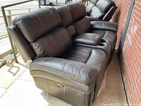 Front angle view of the brown leather power reclining loveseat showing stitching, two seats, and center console with cup holders.