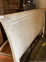 Photo showing the large white wooden headboard of the king size sleigh bed covered with soot and dust, displaying the curved sleigh style and paneled wood design.