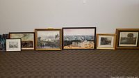 Seven framed prints displayed on floor; diverse subjects including historical architecture and nature scenes.