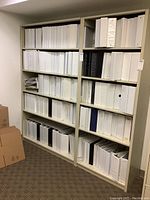 Shelf with multiple rows of white and black binders of various sizes arranged mostly vertically with some haphazardly placed.