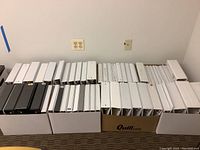 Boxes containing white and black binders in various sizes lined up horizontally.