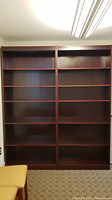 Front view showing two tall, dark brown wood office bookcases with multiple adjustable shelves and minor wear.