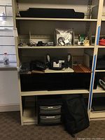 Shelf with various items including keyboards, speakers, storage bins, and bags