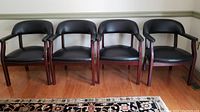 Four black padded Norstar office chairs in a row on a wood floor next to a white wall with green trim