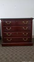 Front view of mahogany wood file cabinet with four brass-handled drawers and glass top