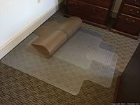 Four clear plastic chair floor mats on carpet, one rolled and three flat, showing shape and protection purpose.