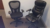 Two office chairs side by side, one mesh-backed and one black leather with visible wear