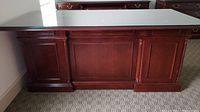 Front view of large dark wood office desk with glass top and paneled drawer fronts