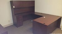 Full view of U-shaped laminate desk unit with hutch showing left-side drawers and desk surface with cord holes