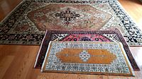 Three rugs stacked, large multicolored, medium and small orange patterned rugs