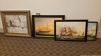 Full view of four framed sailboat-themed paintings arranged on floor, varying in size, color, and framing style.