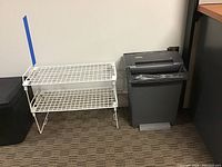 Two-level white metal wire shoe storage shelf standing on a carpeted floor against a white wall.