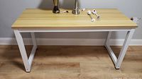 Front view of wood laminate top table with white metal legs on wood floor showing surface wear and scratches.