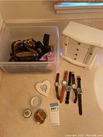 Photo showing small white wooden jewelry box, multiple belts in plastic container, four wristwatches, and small decorative containers including heart-shaped and round floral tins.