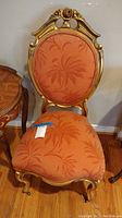 Front view of the vintage style chair showing orange upholstery and carved top with flowers.