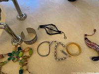 Photo showing multiple bracelets and a beaded necklace on a white surface by a metal pole.