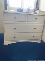 Front view of white vintage dresser showing four drawers with wooden knobs, placed near window