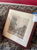 Framed artwork resting on fabric with floral design, showing overall view of the frame and art.