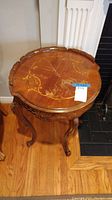 Full view of vintage round side table showing wood inlaid top and carved legs with ram's feet.