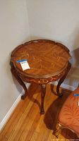 Full view of vintage round side table showing inlaid wood top and carved legs with ram's feet.