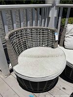 Photo of one outdoor lounge chair showing woven rattan-style curved backrest and light colored cushion with visible dirt and wear.