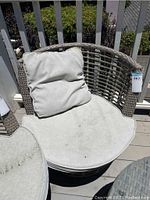 Single outdoor wicker lounge chair with rounded back and beige cushions, showing wear and dirt.