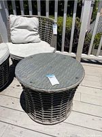 Outdoor round patio table shown from a medium distance, displaying woven rattan style base and dirty glass top.