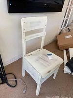 Front view of white wooden storage chair showing seat and backrest with wear marks and discoloration.