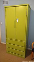 Front view of tall green cabinet showing two doors above and three drawers below.