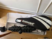 Top view of mobility massage wall device inside box next to Babolat tennis racket cover.