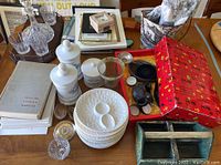 Overview of lot showing vintage glass canisters, glass plates, crystal glasses, vintage book, small frames, red box, and other decorative pieces on a wooden table.