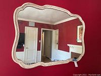 Full view of vintage white carved farmhouse mirror hanging on a red wall, showing its curvy ornate frame and overall condition.