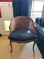 Frontal image of vintage rattan armchair with black cushion showing overall design and structure.