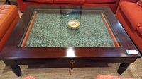 Top down view of the dark wood framed square coffee table with glass top showing the crushed glass inside the drawer beneath.