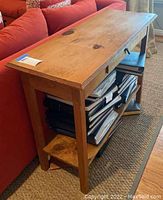 Side angle view showing wood grain, drawer, and lower shelf with storage items.