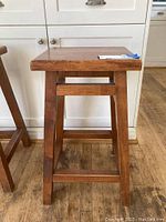 Full view of the wood stool showing its size and structure in front of a white cabinet.
