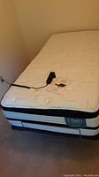 Twin mattress on adjustable bed frame with wired remote control lying on top. Corner showing 'iTwin' mattress branding.