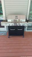Full front view of the Nexgrill deluxe dual energy BBQ grill showing stainless steel lid, multiple control knobs and black storage cabinet with wheels.