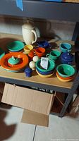 Shelf of assorted Fiesta pieces including covered coffee pot, mugs, bowls, plates and shakers