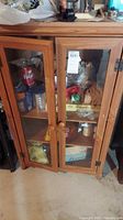 Front view of wooden cabinet with glass doors, showing visible worn spots and nicks. Contents inside cabinet visible but not included.