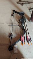 Full view of black compound bow with four arrows in attached holder, placed on concrete floor.