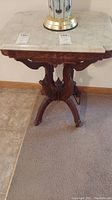 Full view of vintage end table showing rectangular white marble top and ornate dark wooden base with carved leg details.