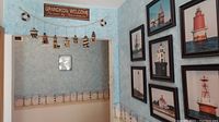 Wide view of nautical themed framed wall art with lighthouse images on blue textured wall, also shows lighthouse garland and welcome sign above opening