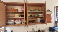 Full view of two kitchen cabinets open showing shelves of glassware, plates and bowls