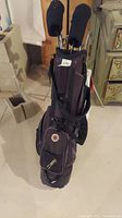 Black golf bag with several golf clubs in it, some clubs covered with black head covers.