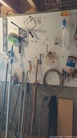 Photo showing a pegboard with various hand tools hung including clamps, long-handled tools, sprayer, hook, coiled wire, screwdrivers, and level.
