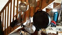 Wide shot showing cast iron skillets, strainers, colanders, and spoons hanging along wooden stairs