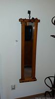 Full front view of tall, narrow, wooden framed mirror mounted on wall.